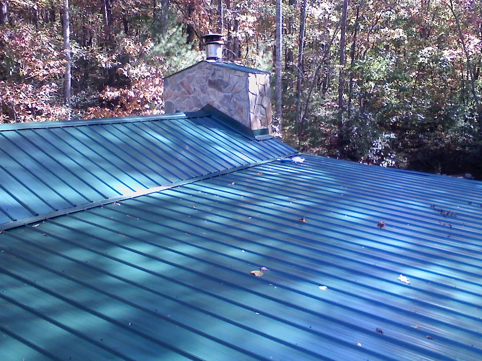 New green metal roof and stone chimney surrounded by autumn woods in Beacon