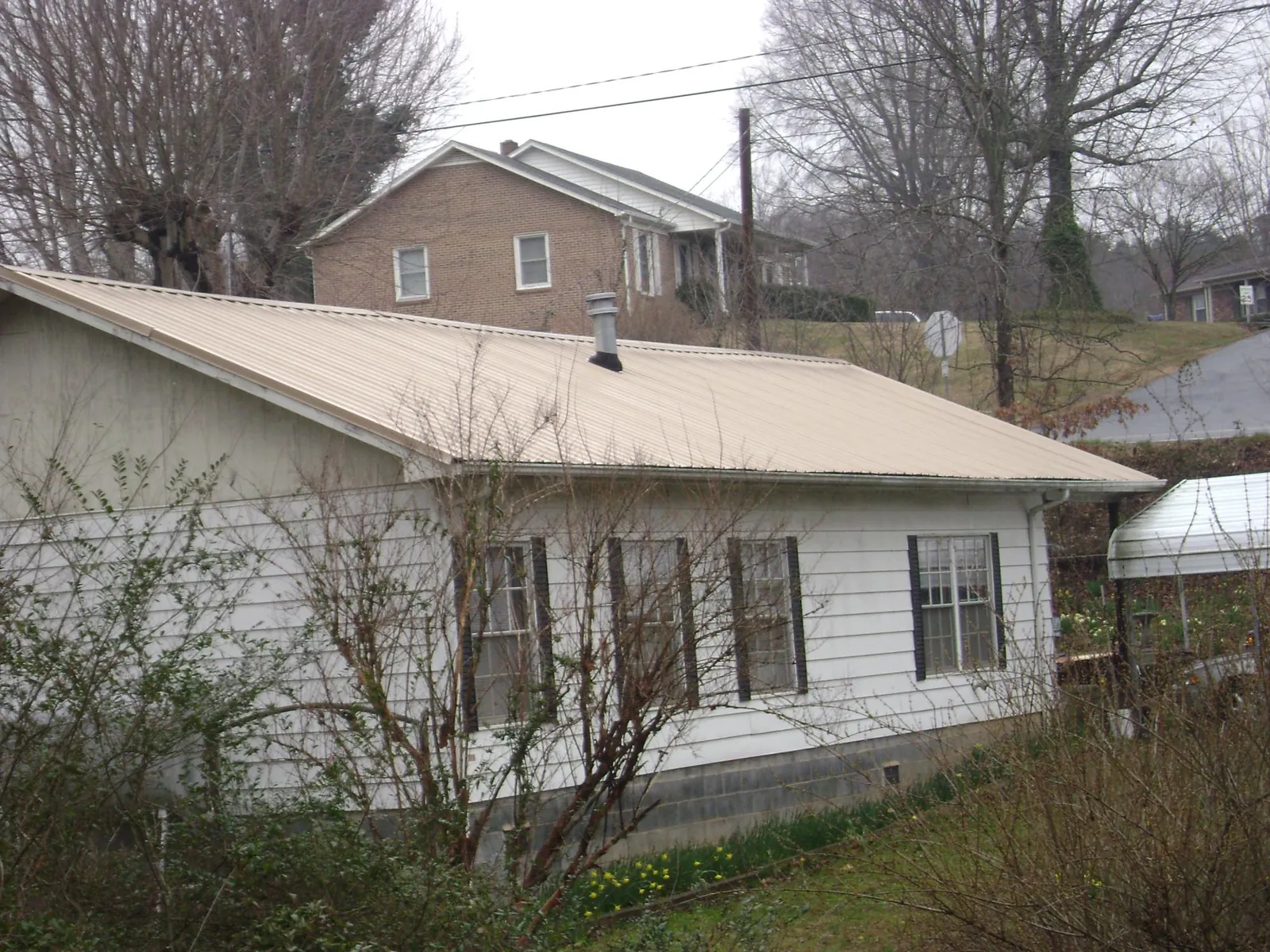 Tan metal roof on a white sided house set into a hillside — Commercial Roofing by Roofing Brothers in Beacon